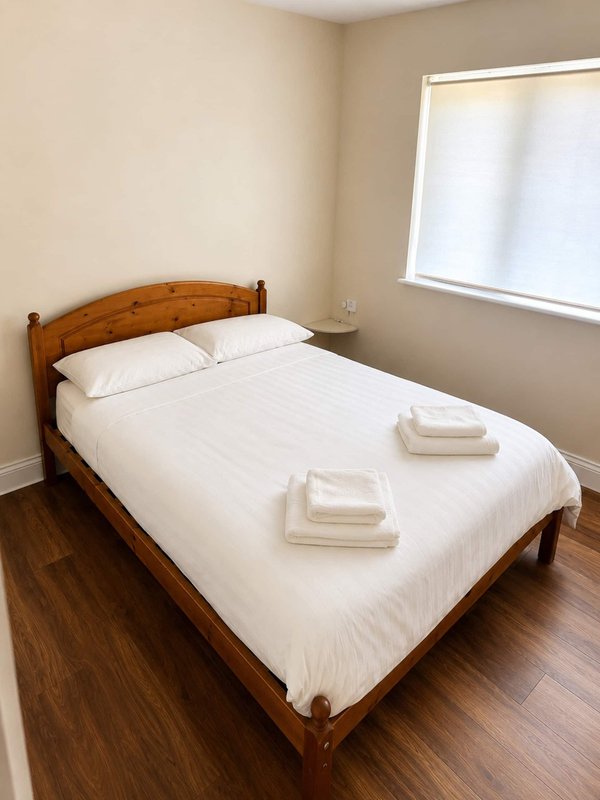 Bedroom with wooden bed frame, white bedding, pillows and towels, wooden floor and window