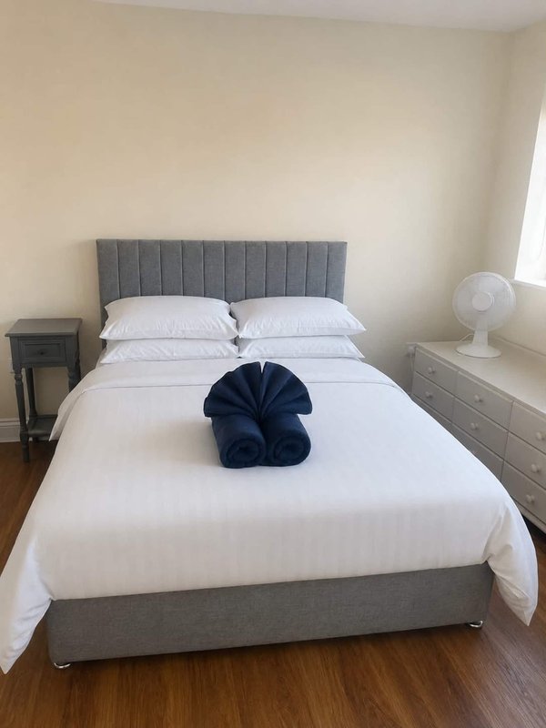 Bedroom with gray upholstered bed, white bedding, decorative blue pillow, and wooden floor