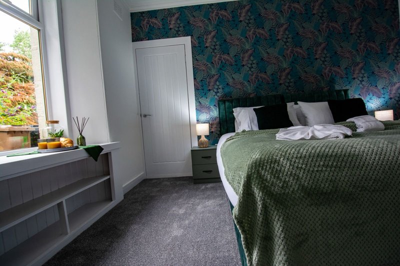 Bedroom with double bed, green bedding, dark patterned wallpaper, window and door