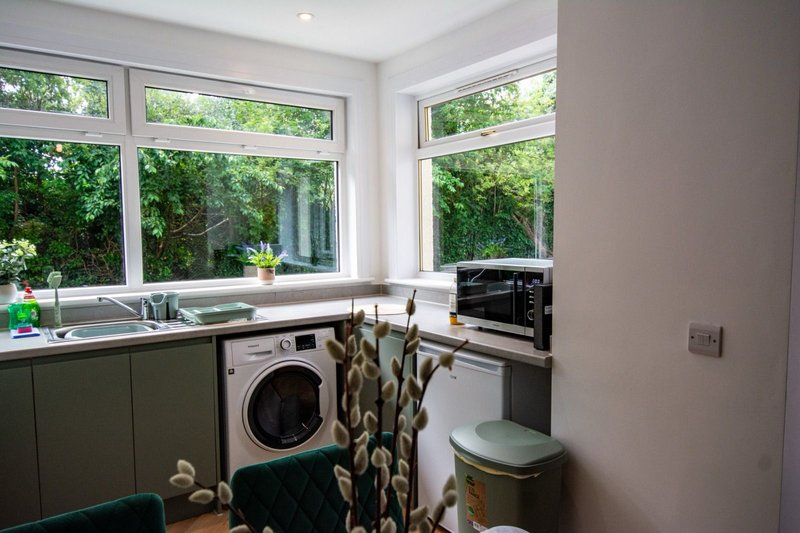 Modern kitchen with washing machine, oven, and large windows overlooking garden