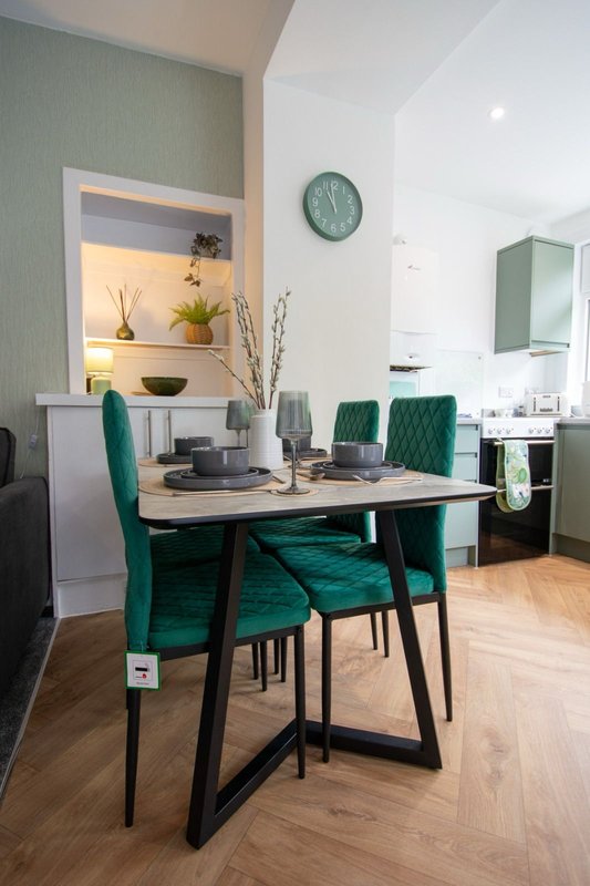 Modern dining area with wooden table, green velvet chairs, wall niche and kitchen beyond