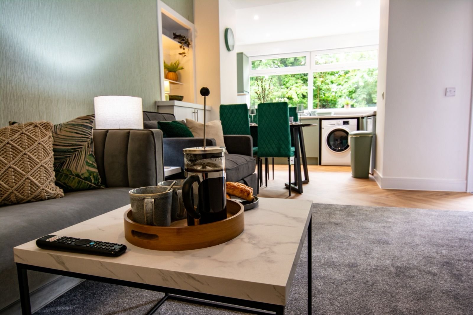 Modern open-plan living room with sofa, dining chairs, wooden coffee table and washing machine visible
