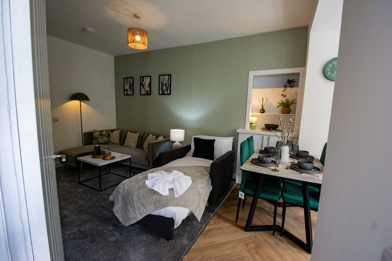 Studio apartment with sofa, bed, desk, and seating area in sage green and neutral tones