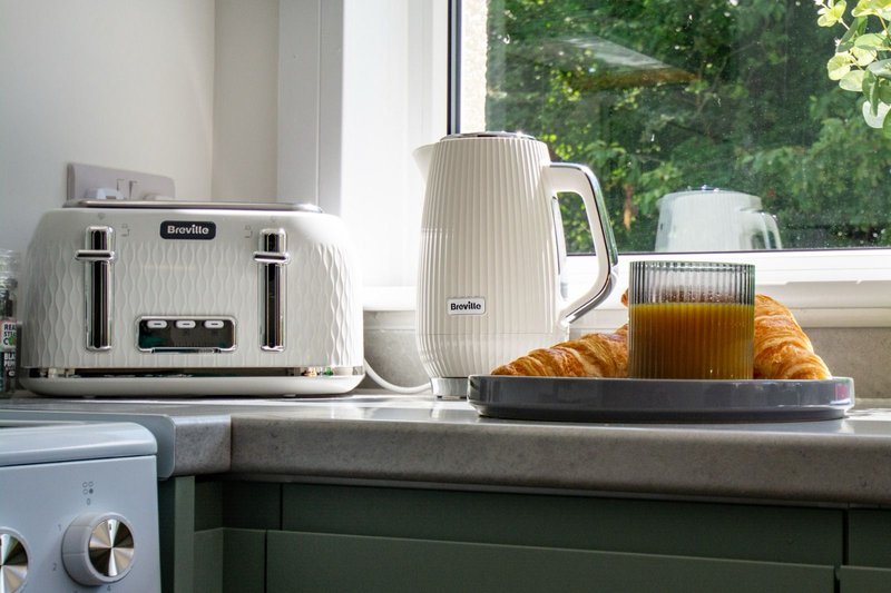 Kitchen counter with white toaster, kettle, and breakfast items by window with garden view