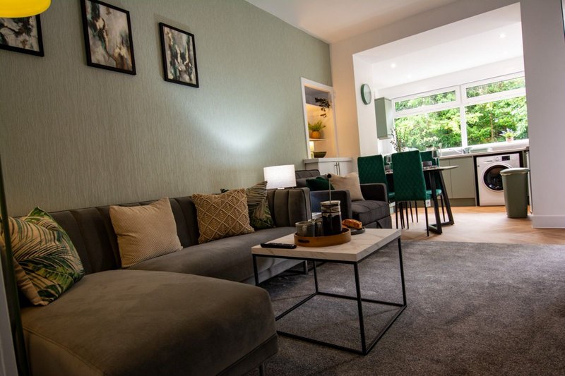 Open-plan living room with grey sofa, coffee table, and kitchen area visible through doorway