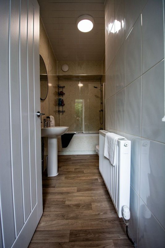Modern bathroom with pedestal sink, shower enclosure, towel rail and wooden flooring