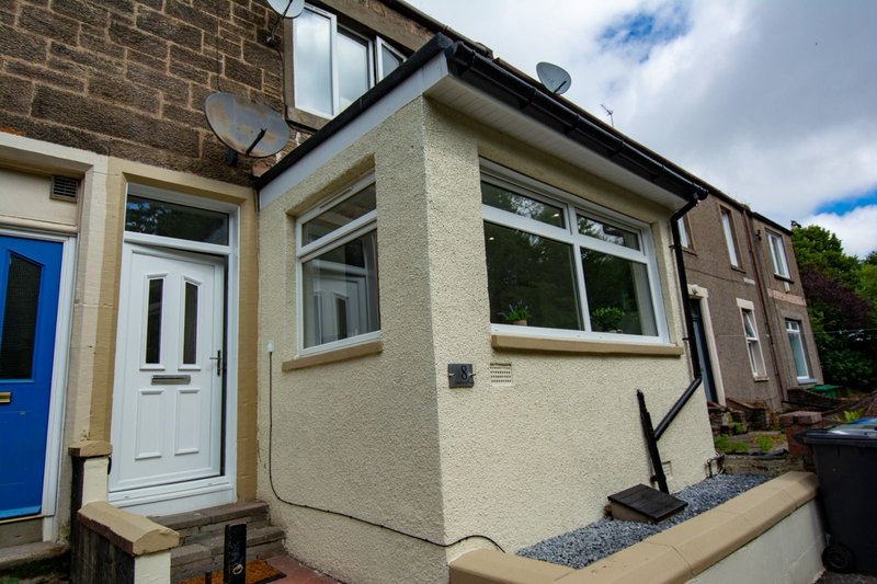 Cream-rendered bungalow exterior with blue door, white entrance, large windows and gravel garden