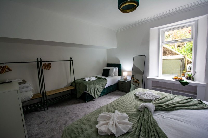 Bright bedroom with two beds, white walls, large window with garden view, and green bedding