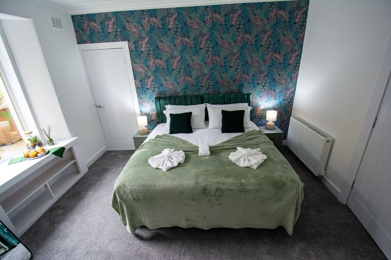 Bedroom with double bed, green bedspread, patterned teal wallpaper, white pillows and towels