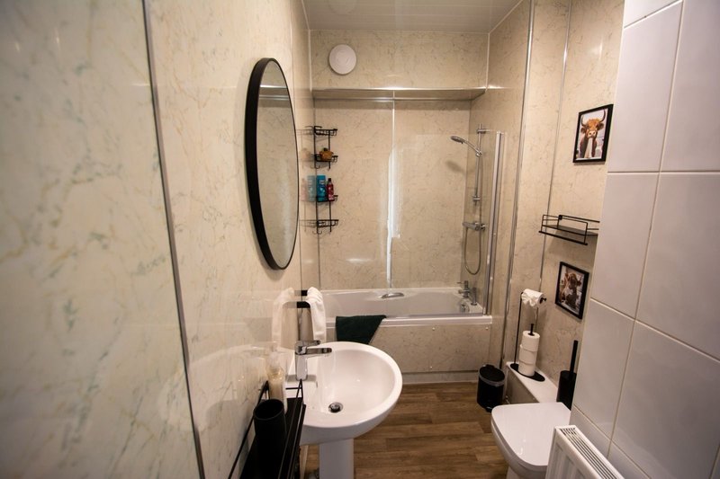 Modern bathroom with pedestal sink, round mirror, shower enclosure and white tile walls