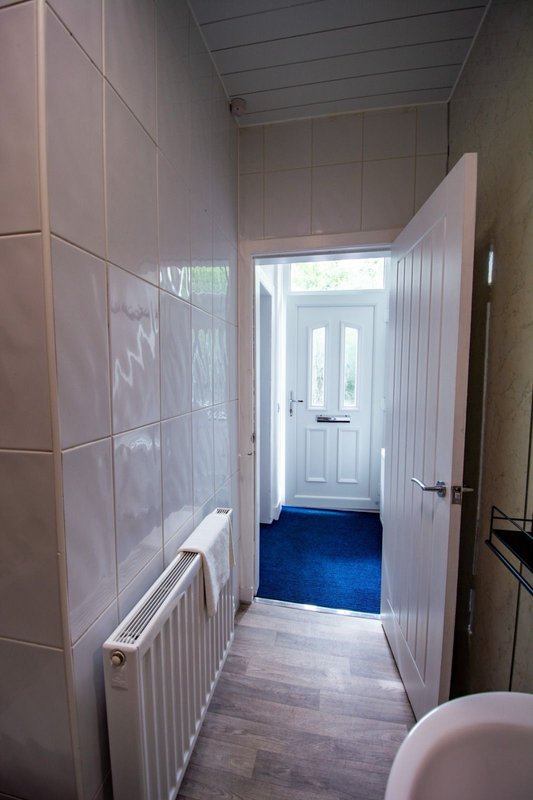 Bathroom hallway with tiled walls, radiator, wooden floor and open door to entrance