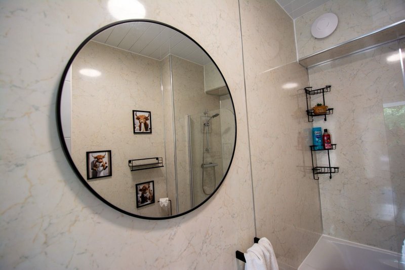 Modern bathroom with round mirror, shower enclosure, and marble-effect tiles