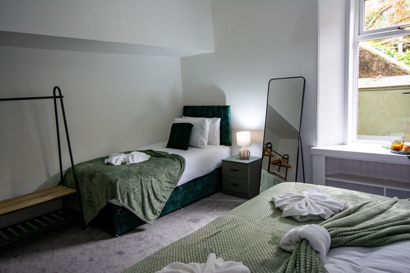 Bedroom with two beds, green bedding, mirror, nightstand and window with garden view