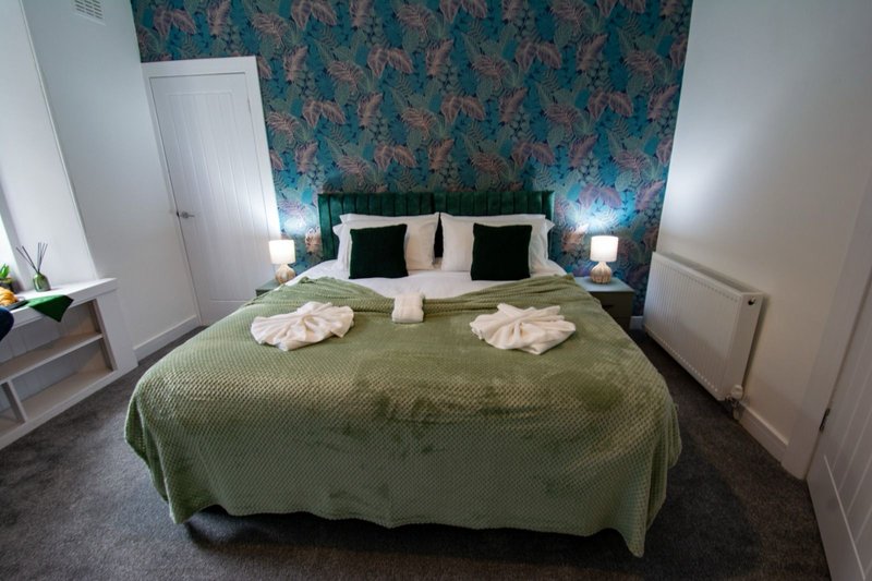 Bedroom with double bed, green bedspread, patterned teal headboard wall, and side lamps