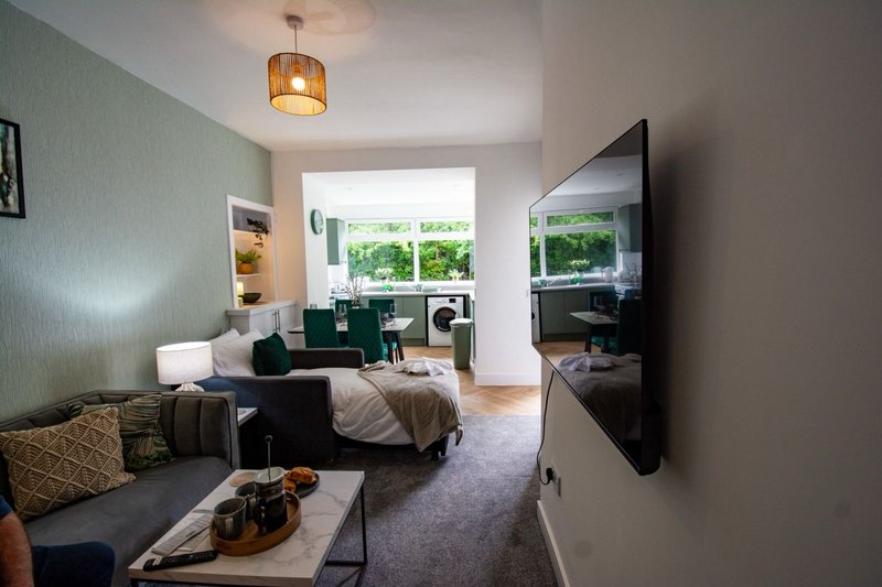Modern living room with sofa, desk area, wall-mounted TV, pendant light and garden views