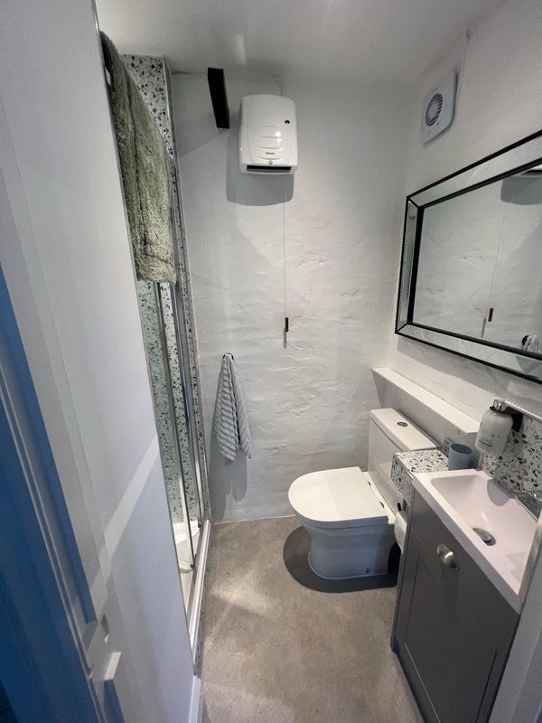 Small bathroom with toilet, sink, mirror, and wall-mounted soap dispenser