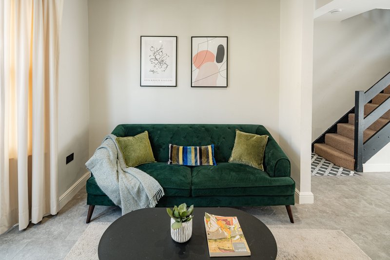 Living room with green velvet sofa, yellow cushions, throw blanket, round black table and framed wall art