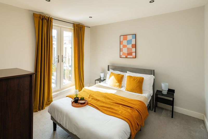 Bright bedroom with double bed, yellow bedding and cushions, wooden furniture and gold curtains