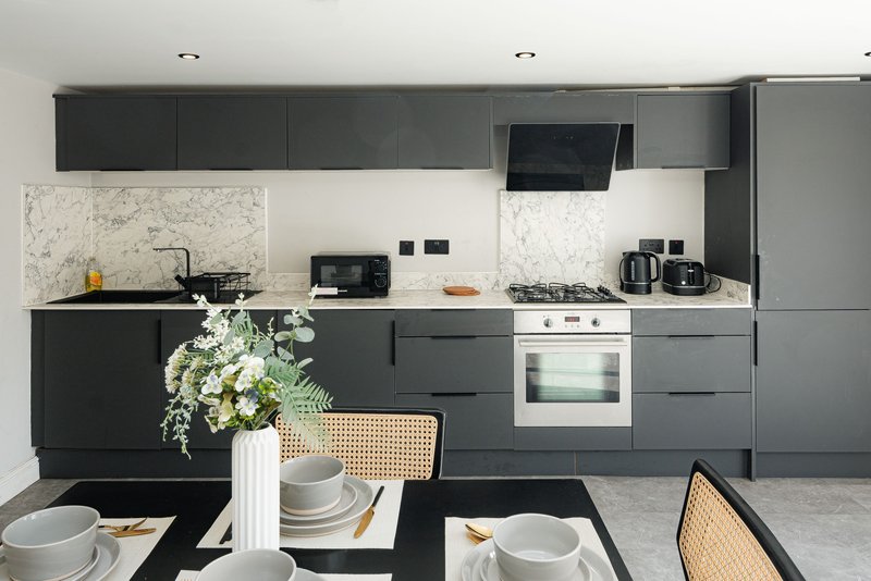 Modern kitchen with dark cabinetry, marble backsplash, stainless steel appliances and dining table