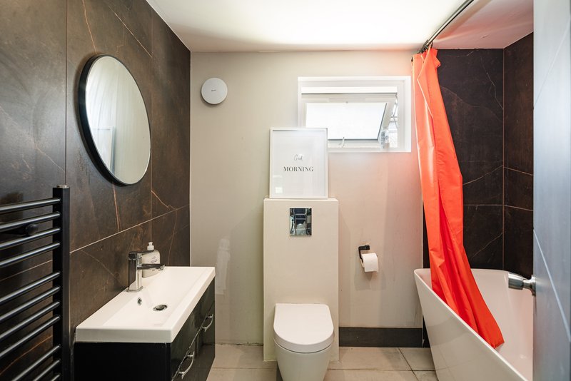 Modern bathroom with dark tile walls, white sink, toilet, bathtub and round mirror