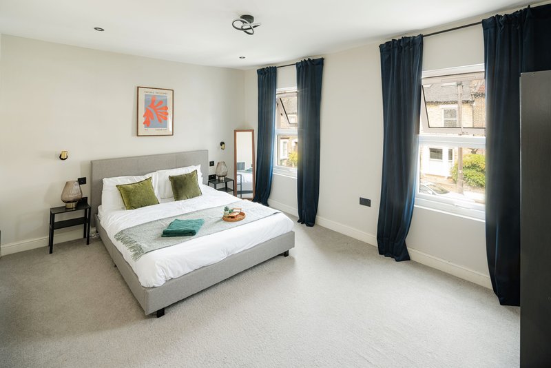 Bright modern bedroom with grey bed, navy curtains, white bedding and framed wall art