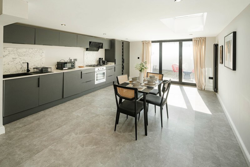 Modern open-plan kitchen and dining area with gray cabinetry, marble backsplash, dining table and large windows