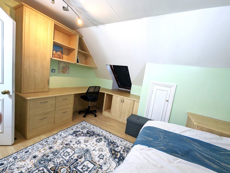 Bright bedroom with wooden desk, chair, bed with blue bedding, and green accent wall