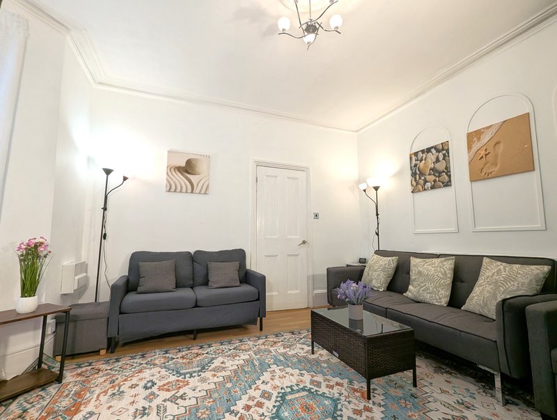 Bright living room with two gray sofas, patterned rug, wall art, and floor lamps