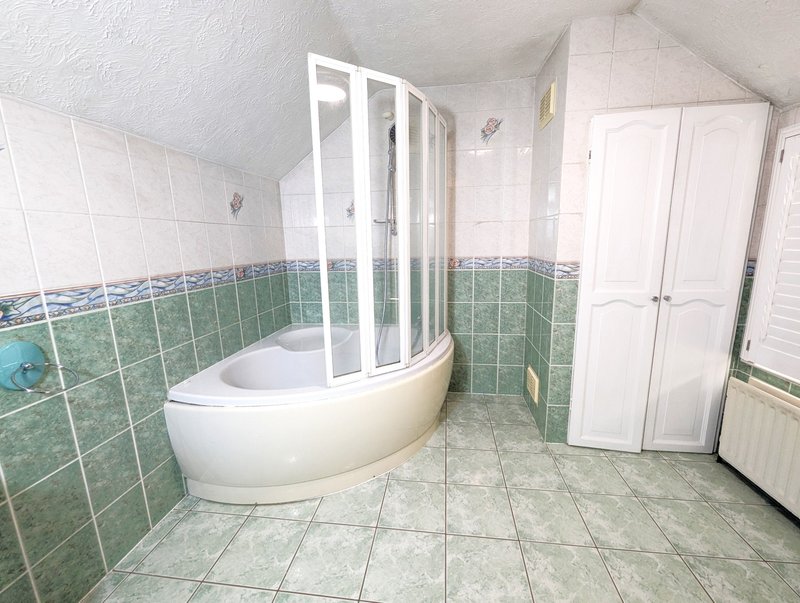 Spacious bathroom with curved corner bathtub, shower enclosure, white cabinetry and green tile