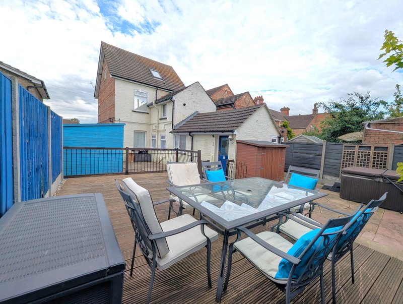 Outdoor patio with dining table, chairs, and blue gate overlooking residential street