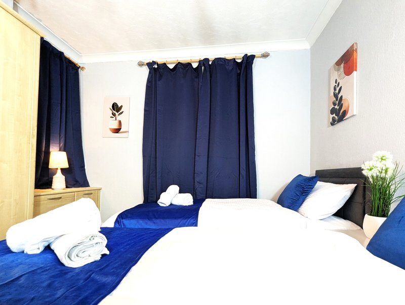 Bright bedroom with two single beds, blue bedding, dark curtains and white walls