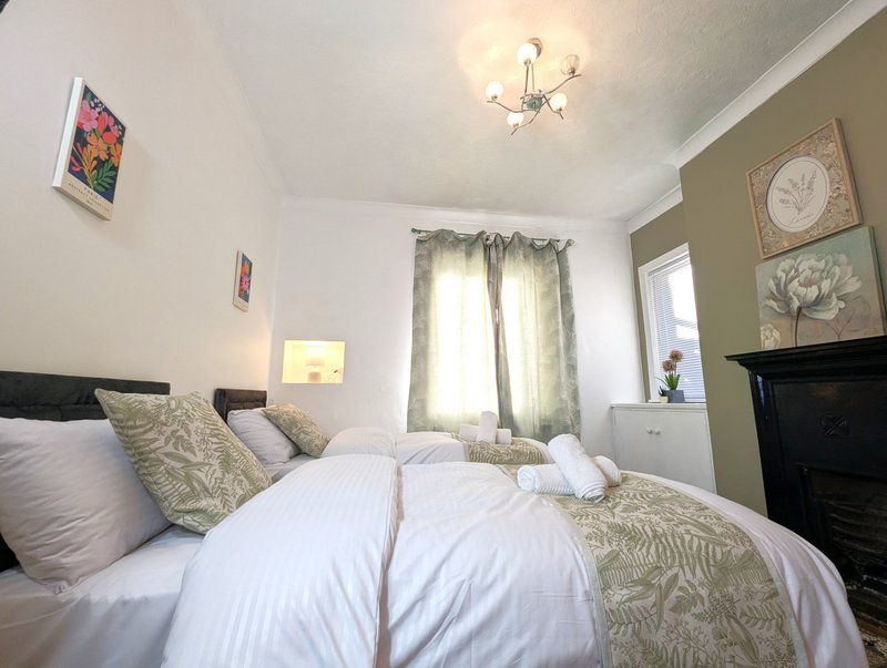 Bright bedroom with double bed, white bedding, decorative pillows, and framed botanical wall art.