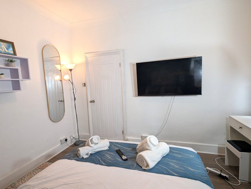 Bedroom with double bed, wall-mounted TV, mirror, floor lamp and towels