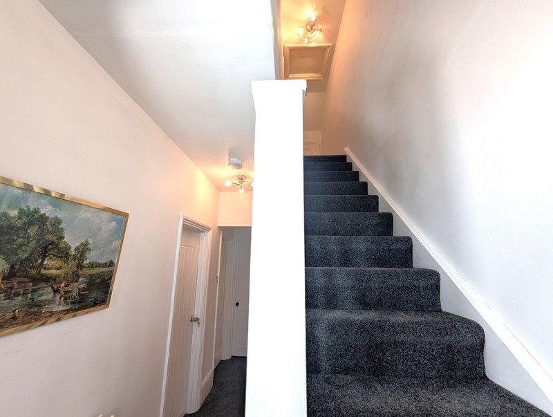 Hallway with staircase, white walls, framed landscape painting, and warm lighting