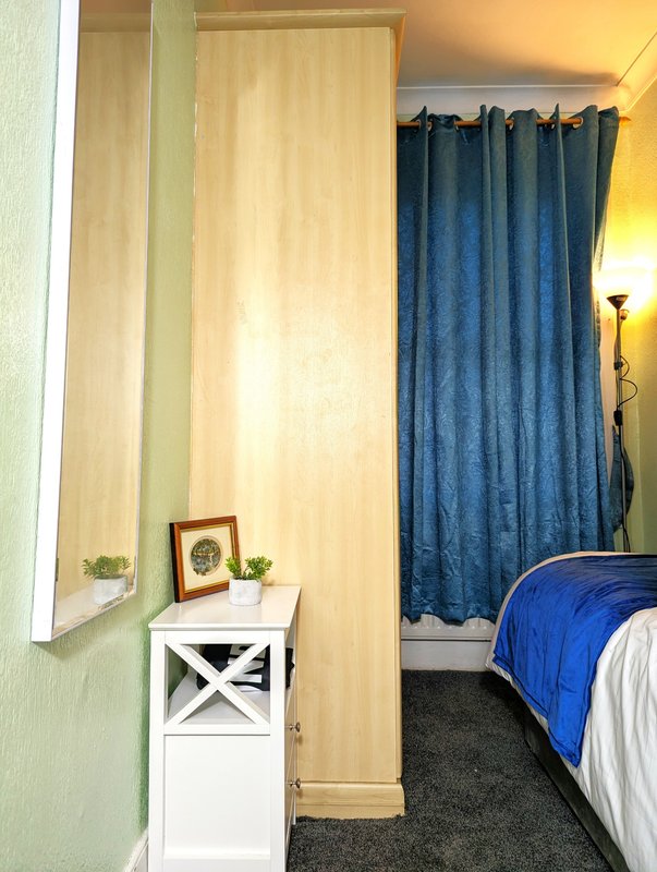 Narrow bedroom with single bed, white storage cabinet, framed portrait and potted plant