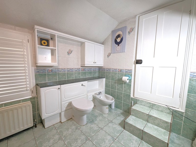 Bathroom with toilet, sink, green tile walls, white cabinetry and bright window