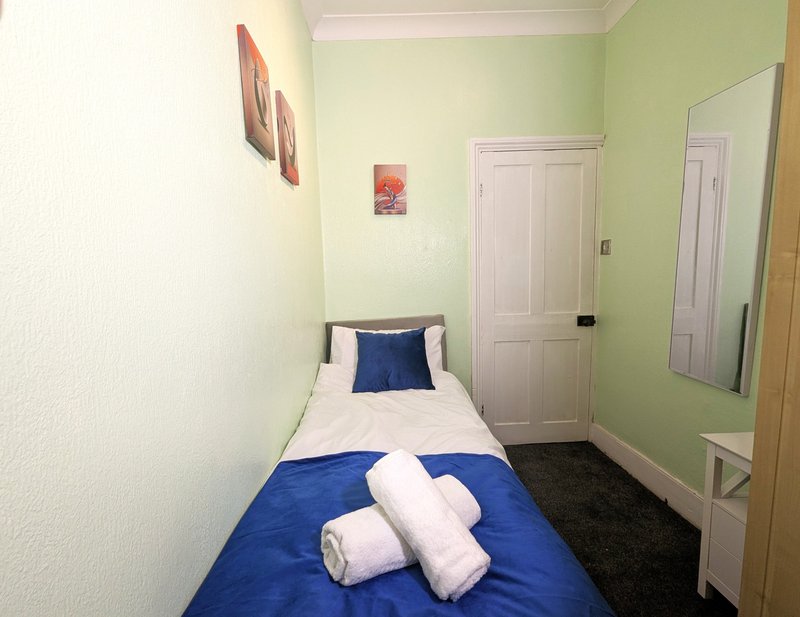 Narrow bedroom with single bed, blue duvet, white pillows, green walls and white doors