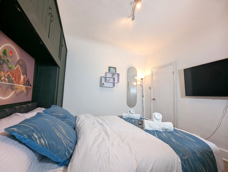 Bedroom with double bed, blue pillows, wall-mounted TV, and modern lighting fixtures