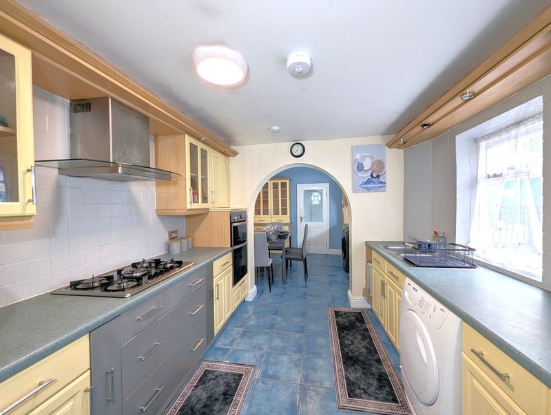 Galley kitchen with wooden cabinets, gas hob, stainless steel appliances and blue flooring.