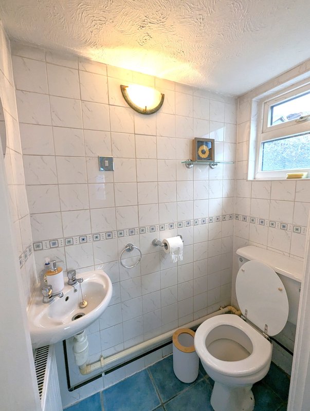 Small bathroom with white tile walls, sink, toilet, and wall-mounted lighting fixture