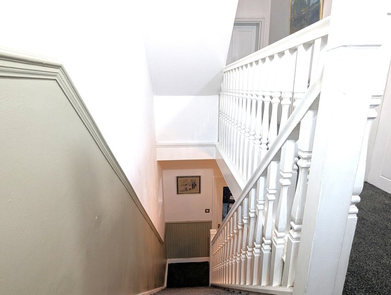 Stairwell with white bannister, pink walls, and carpeted landing below