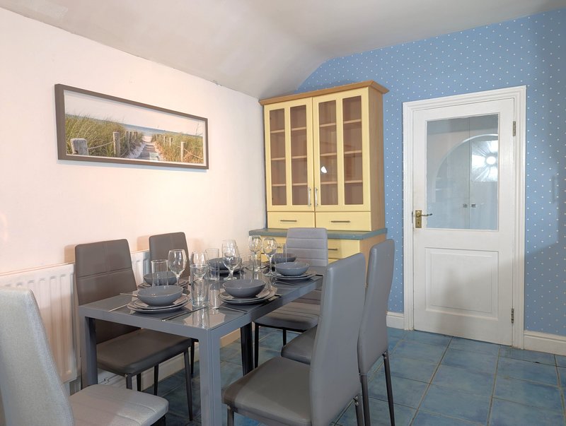 Dining area with black table, grey chairs, yellow cabinet, and blue wallpaper
