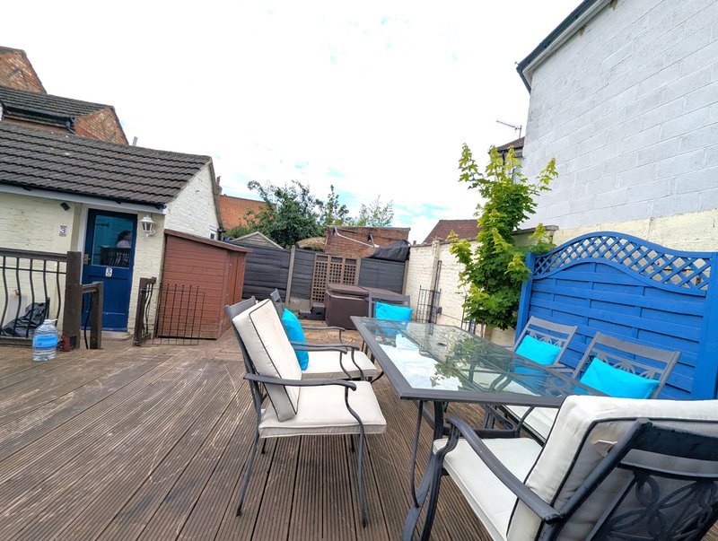 Outdoor decking area with garden furniture, blue fence, and brick buildings