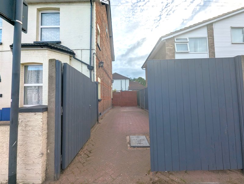 Narrow outdoor side passage between residential buildings with metal fencing