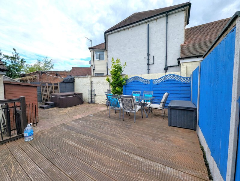 Spacious outdoor deck with patio furniture, blue fence, and white house behind