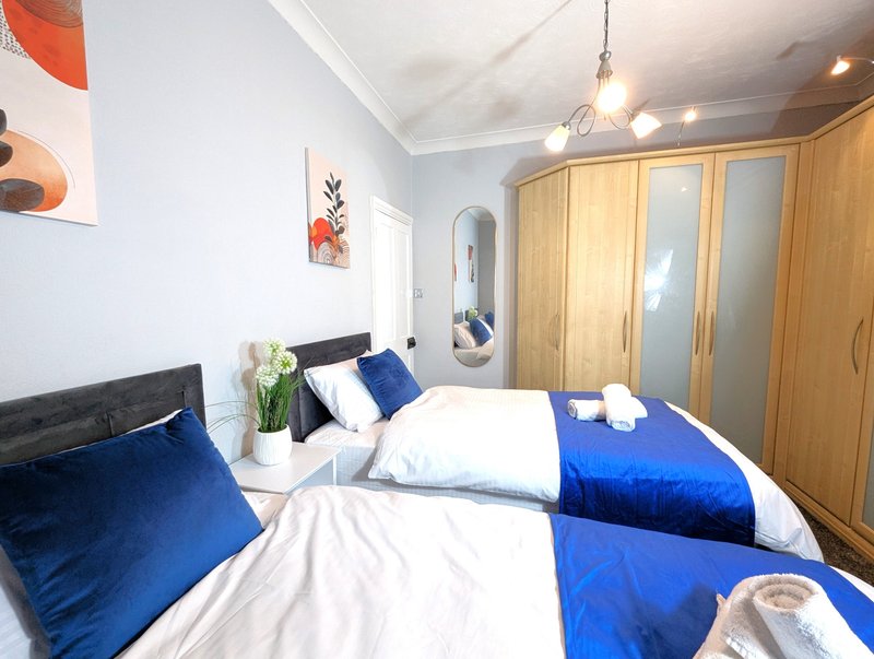 Modern bedroom with twin beds, blue bedding, wooden wardrobes, and pendant lighting