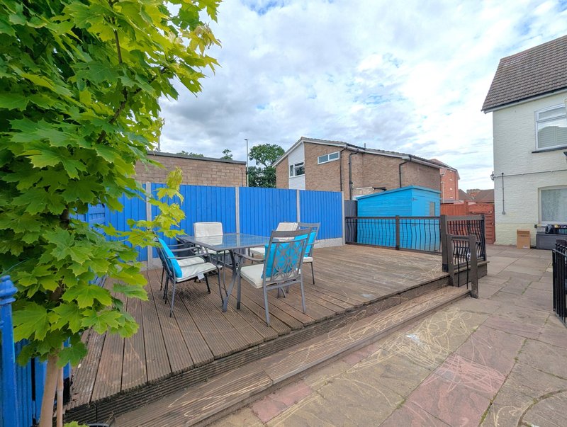 Outdoor patio area with blue fencing, wooden decking, seating, and surrounding residential buildings