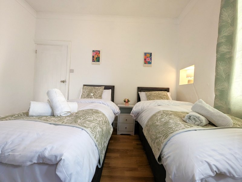 Twin bedroom with two single beds, wooden floor, white walls and small wall art