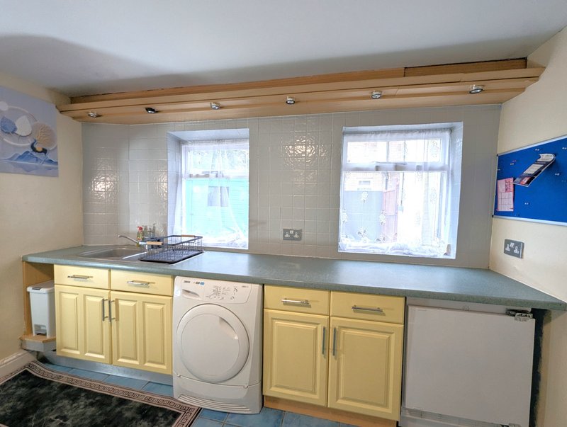 Utility room with yellow cabinets, washing machine, sink and countertop workspace