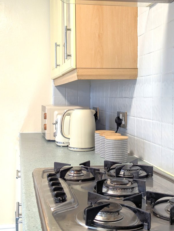 Kitchen with gas cooktop, cream kettle, wooden cabinets and white tile backsplash